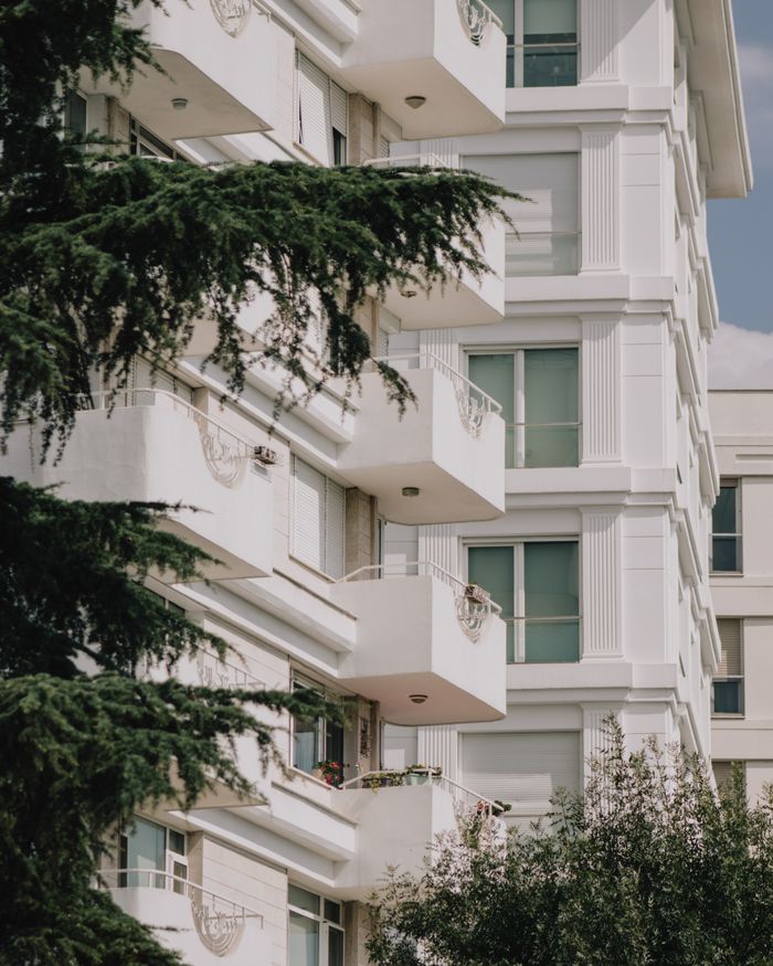Services Stylish white apartment building with balconies nestled among greenery.