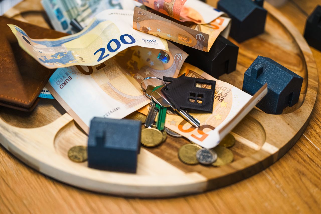 1 Euro currency, keys, and miniature houses symbolize real estate and finance concepts.