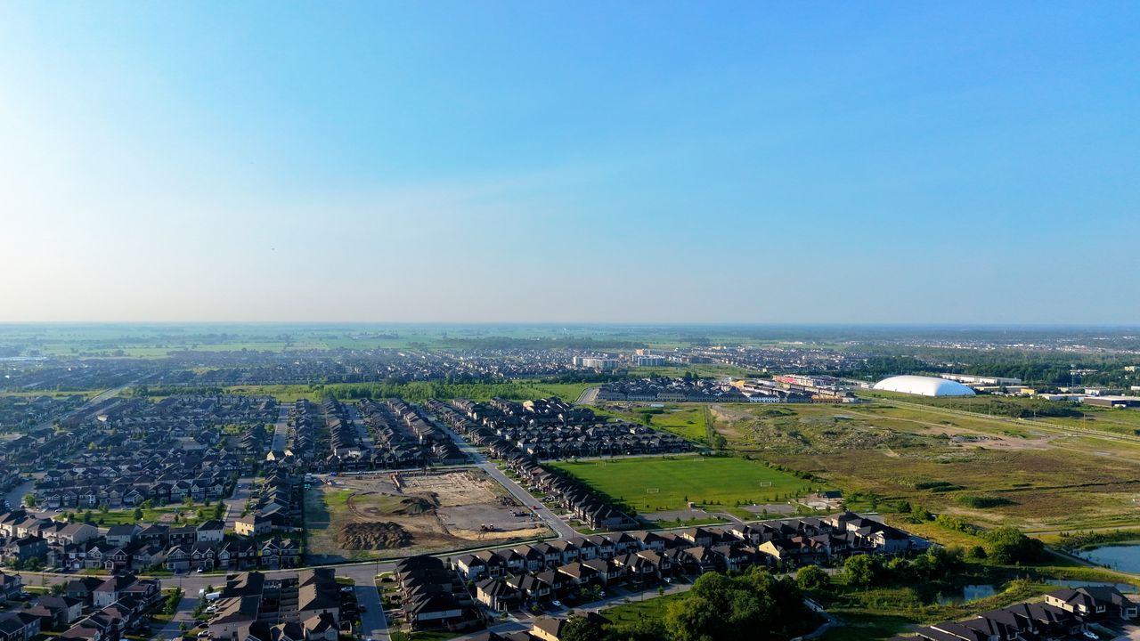 Aerial view showcasing suburban houses, green fields, and open sky.