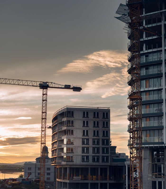 A construction site in Bratislava with cranes and buildings under a sunset sky.